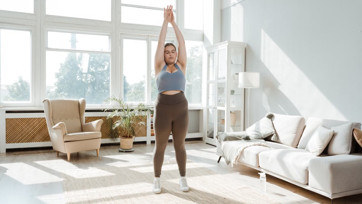 A woman practices stretching exercises in a sunlit living room, promoting wellness and healthy lifestyle.